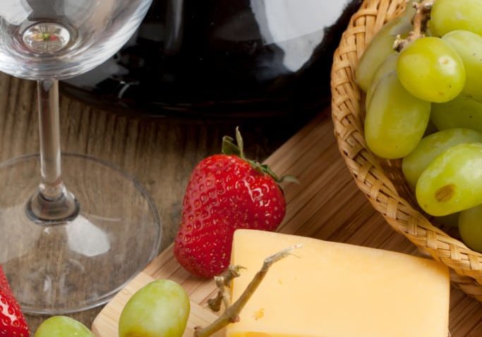 Red wine in decanter with grapes, strawberries and cheese on old wooden table