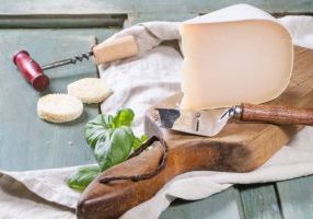 Goat cheese, served with fresh basil and bread on wooden cutting board over turquoise wooden table.